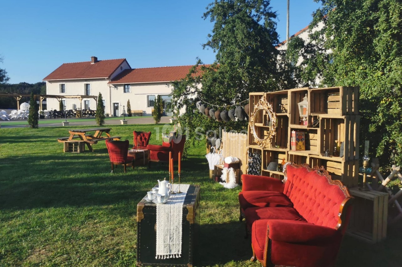 Mobilier vintage avec fauteuils rouges et décorations en bois disposés sur une pelouse devant des bâtiments.