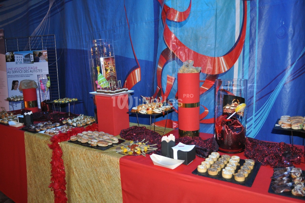 Buffet décoré avec des plats variés, des desserts et des décorations rouges sur une nappe dorée et rouge.