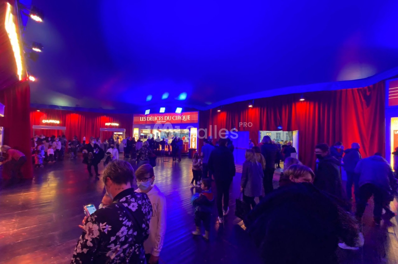 Foule rassemblée dans un espace intérieur éclairé en bleu et rouge, avec des stands lumineux en arrière-plan.