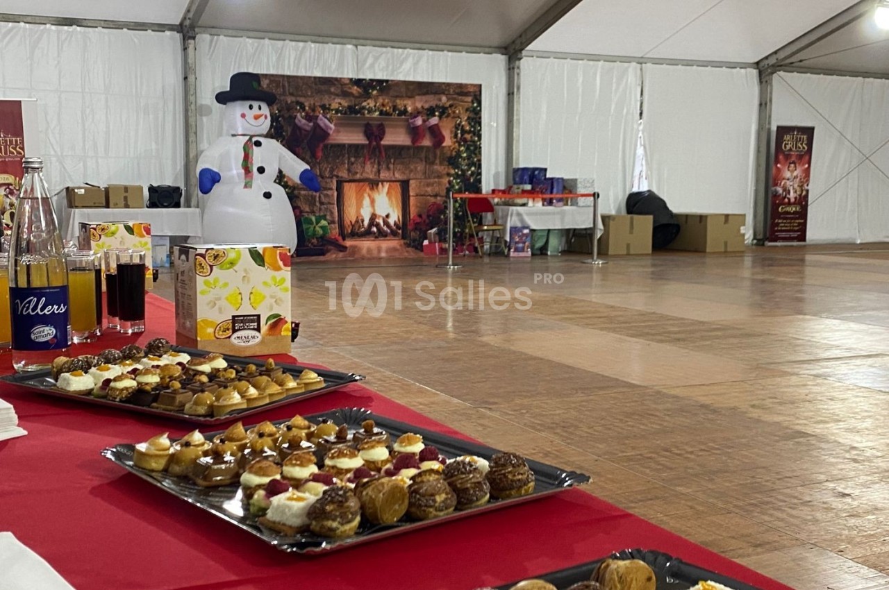 Plateaux de pâtisseries sur une table rouge dans une salle décorée avec un bonhomme de neige gonflable et une cheminée en…