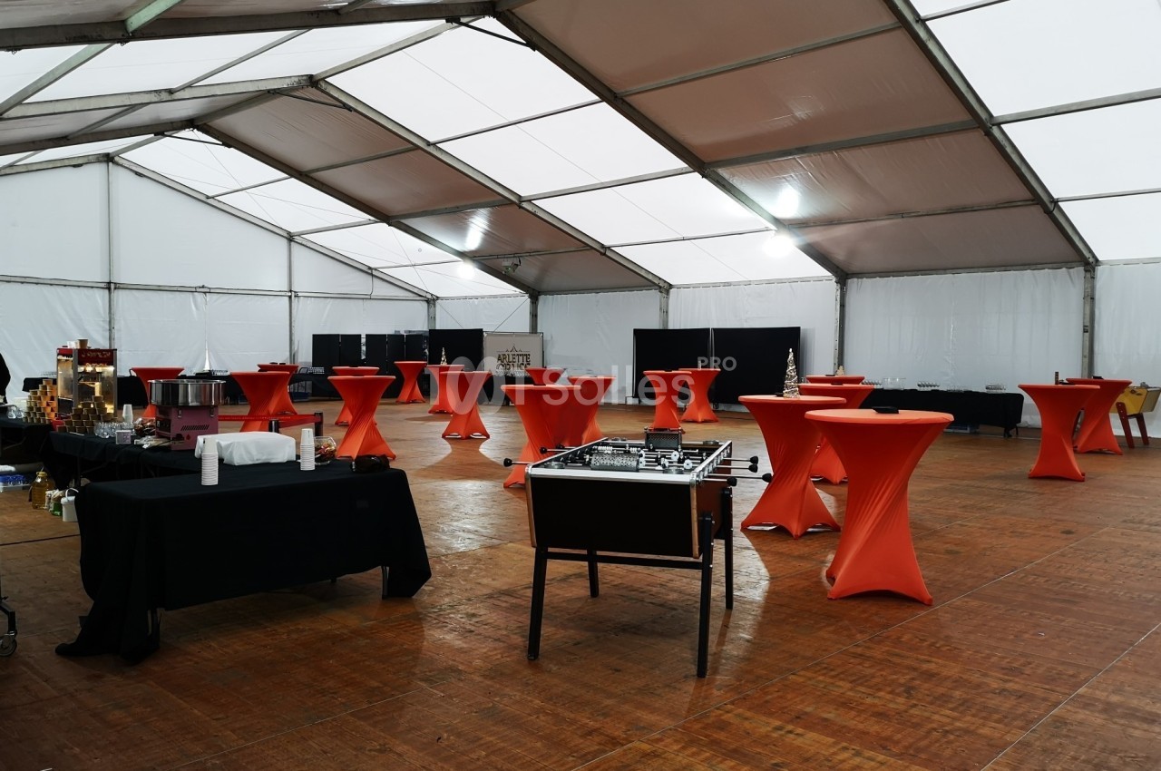 Grande tente aménagée avec des tables hautes recouvertes de nappes rouges, un baby-foot et des buffets noirs.