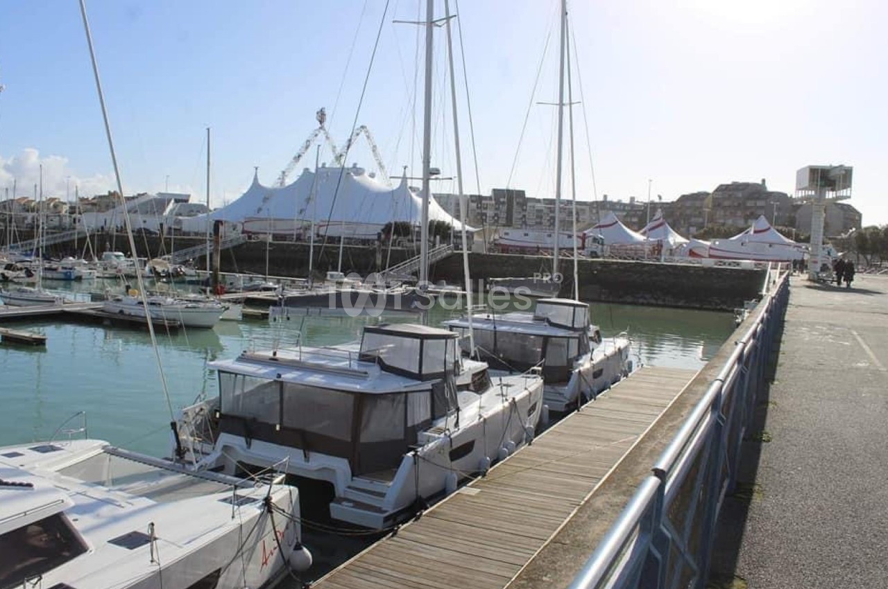 Des catamarans amarrés dans un port, avec des tentes blanches et des bâtiments en arrière-plan.