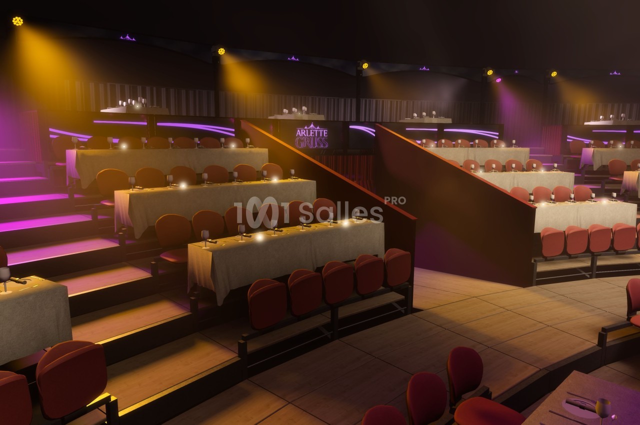 Salle de spectacle avec gradins, tables dressées et éclairage coloré créant une ambiance chaleureuse.