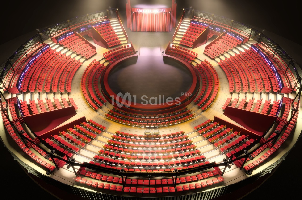 Vue d'un théâtre circulaire avec des rangées de sièges rouges entourant une scène centrale éclairée.