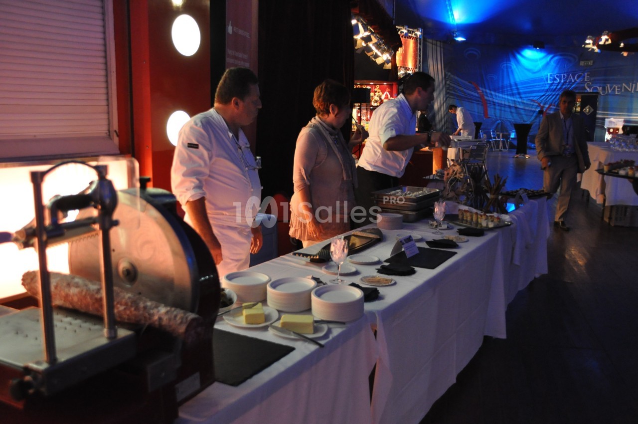 Des chefs préparent un buffet avec des plats variés sur une table dans une salle éclairée.