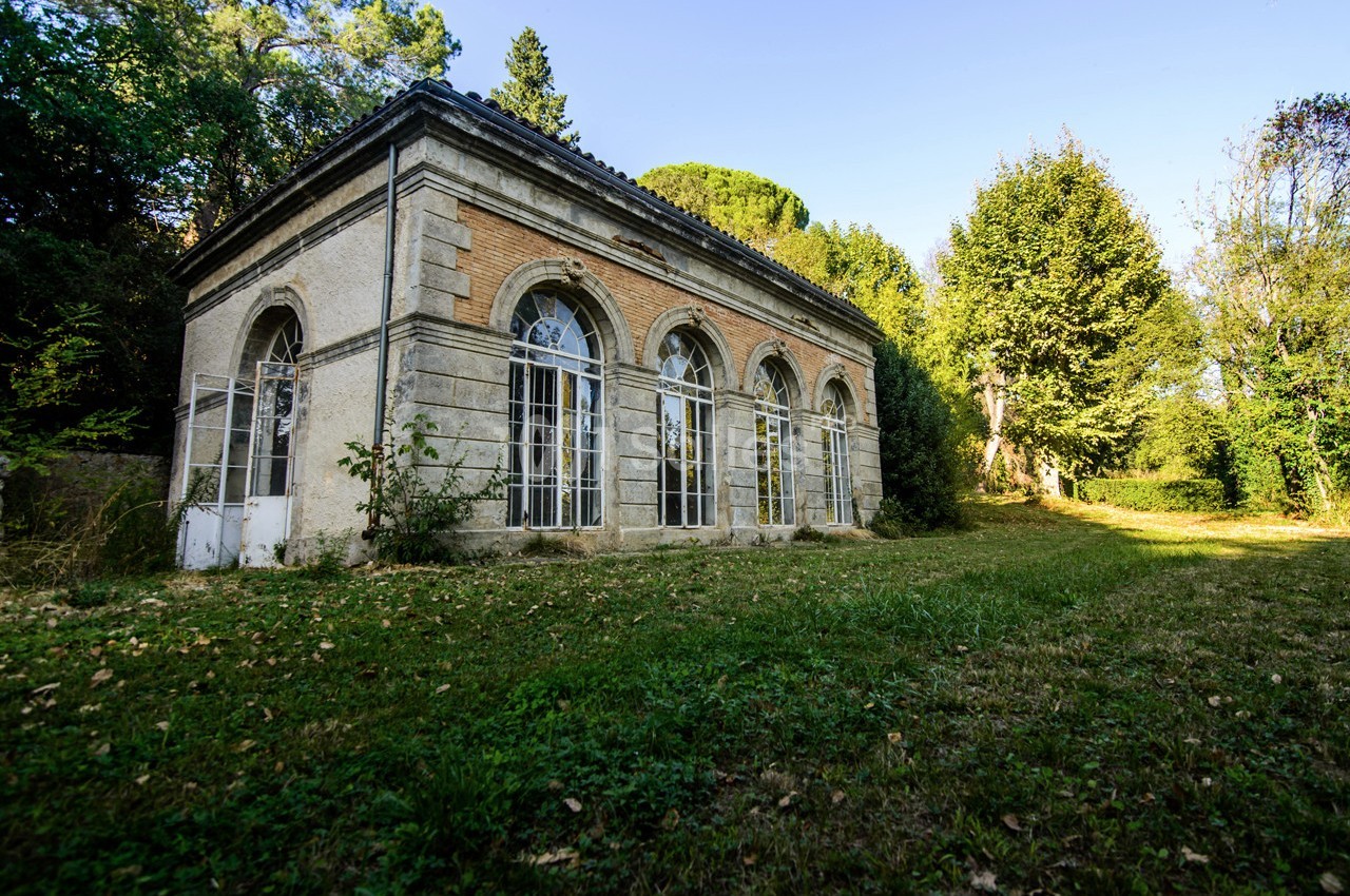 Bâtiment ancien en pierre et brique avec de grandes fenêtres cintrées, entouré de verdure et d'arbres.
