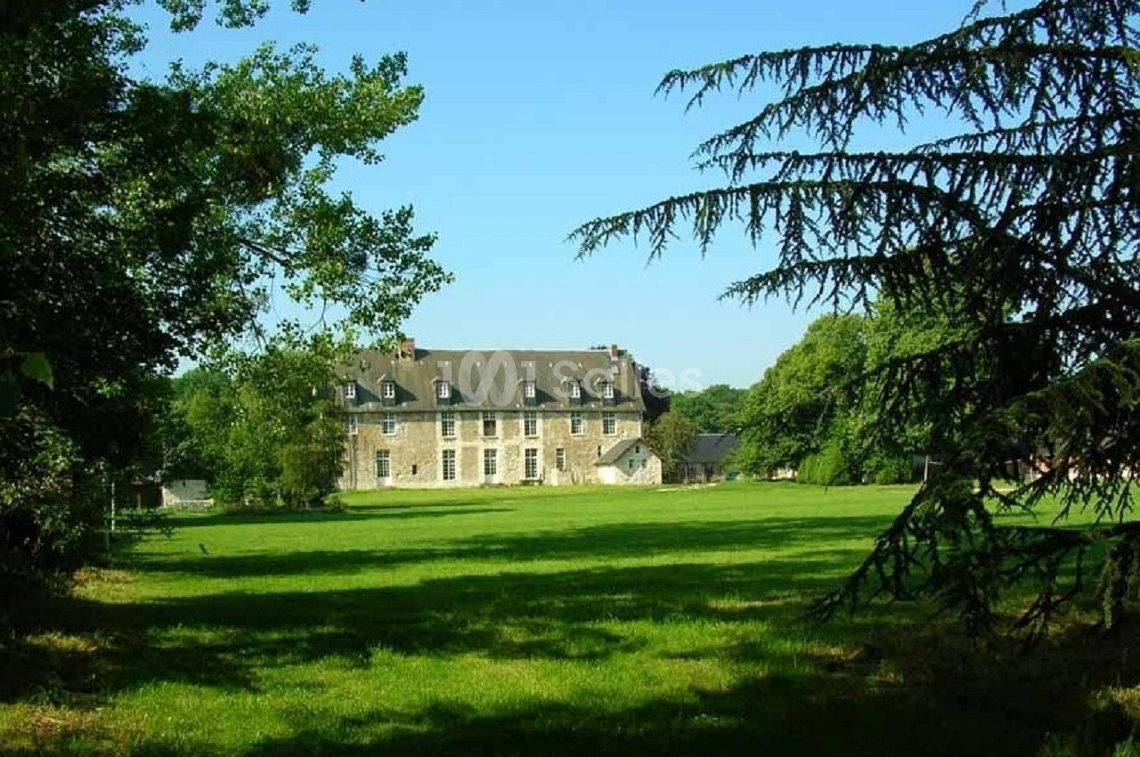 Manoir en pierre entouré d'une pelouse verdoyante et d'arbres sous un ciel bleu clair.