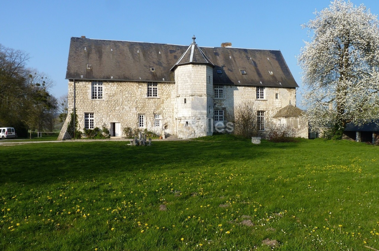 Bâtiment en pierre ancienne avec une tourelle centrale, entouré d'une pelouse et d'un arbre en fleurs.