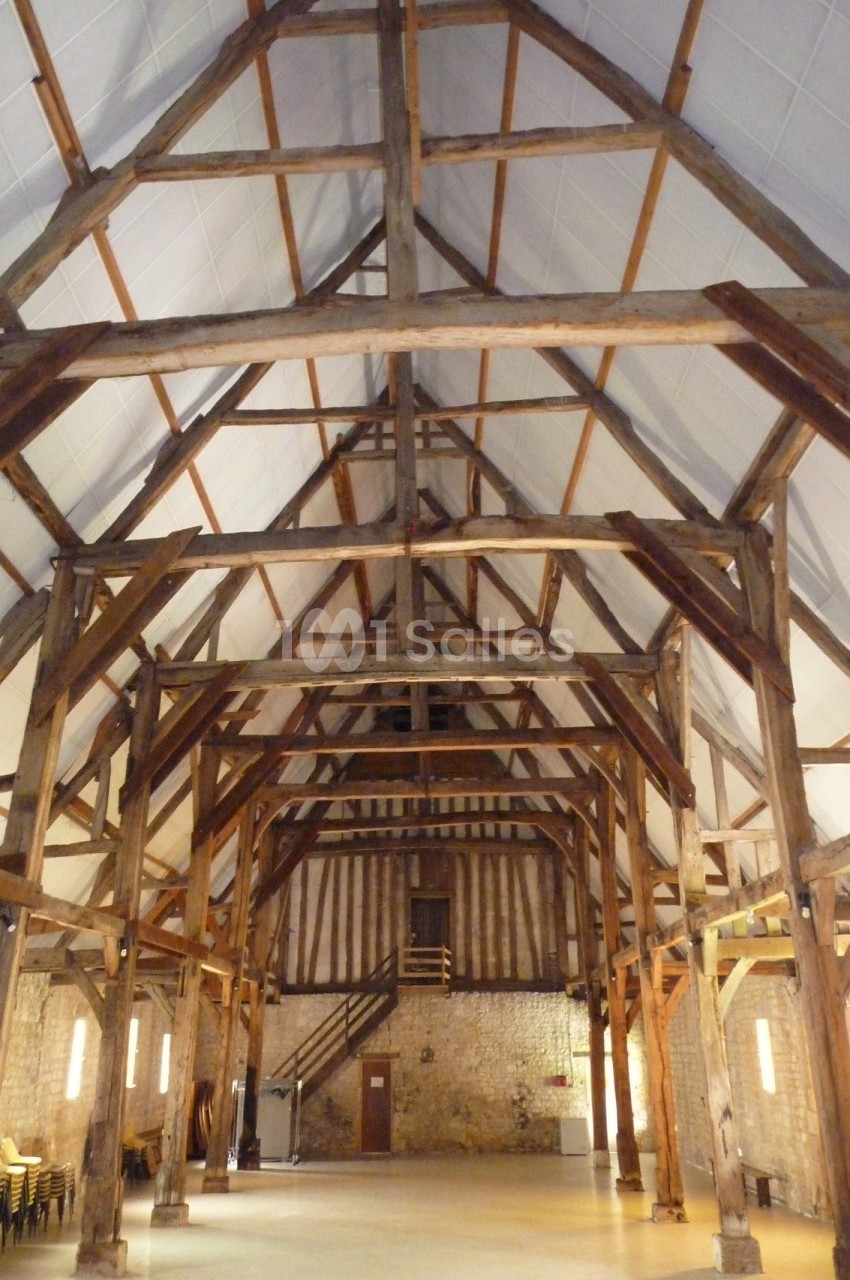 Charpente en bois apparente d'une grande salle avec murs en pierre et éclairage mural discret.