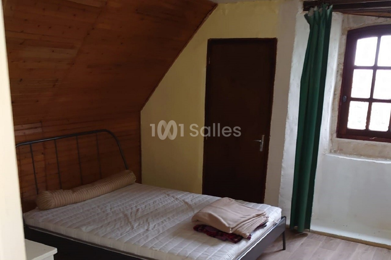 Chambre mansardée avec un lit simple, une fenêtre à rideaux verts, un mur en bois et une porte en bois foncé.