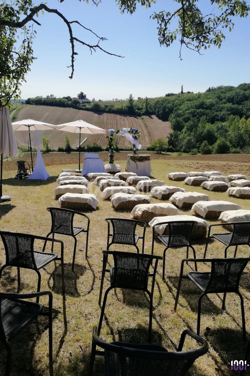Chaises et bottes de paille disposées en extérieur pour une cérémonie, avec vue sur des champs et des collines verdoyantes.