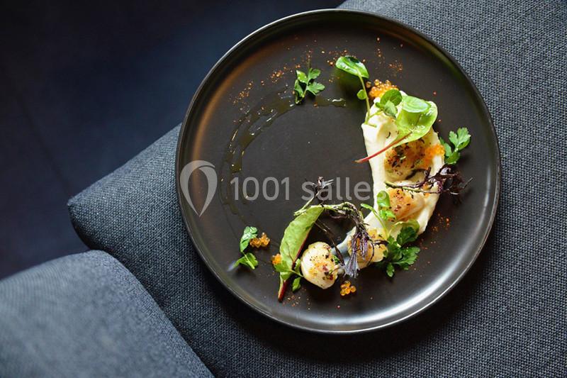 Assiette gastronomique avec des coquilles Saint-Jacques, herbes fraîches et garnitures colorées sur une table sombre.