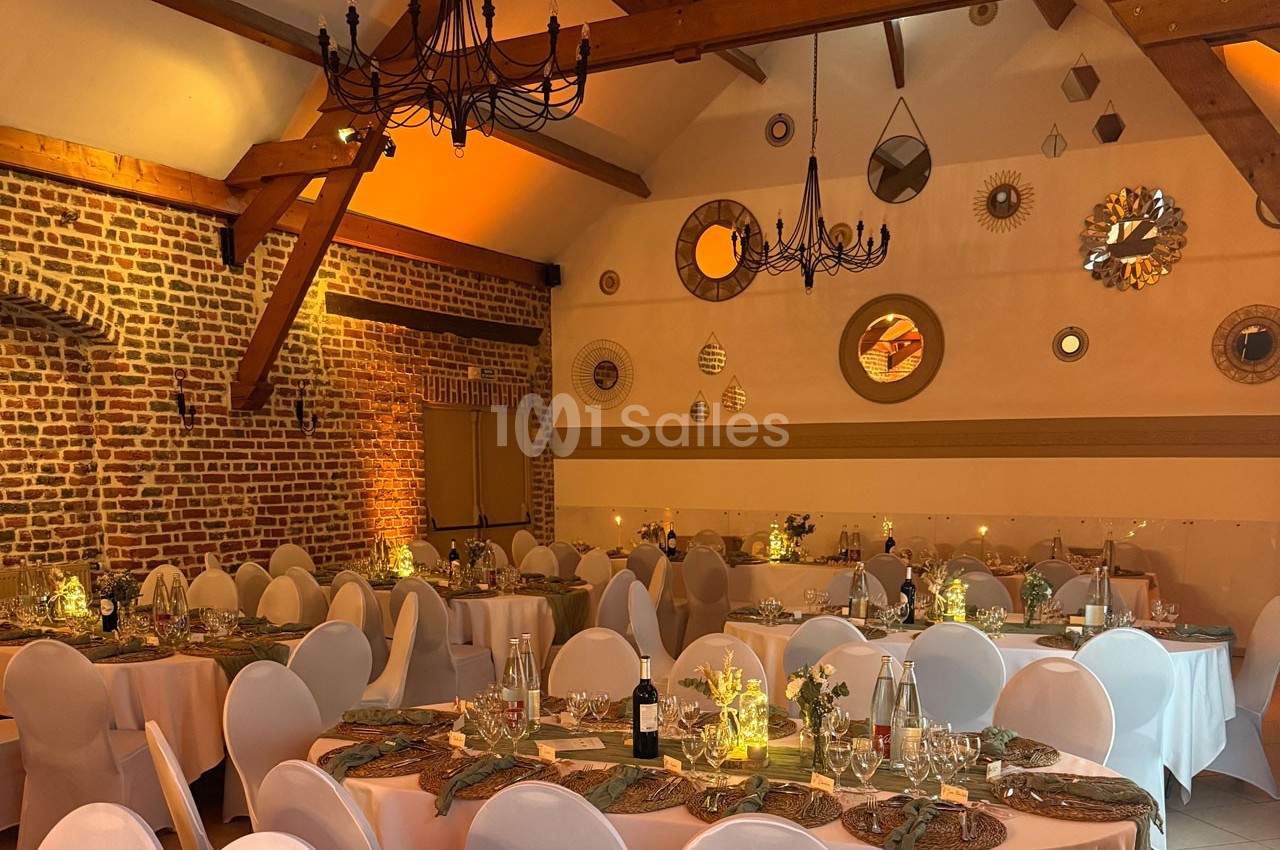 Salle de réception décorée avec des tables dressées, des chaises blanches et des lumières tamisées sous un plafond en…