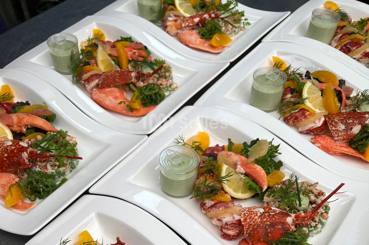 Assiettes de homard avec légumes, agrumes, salade et sauce verte, soigneusement dressées sur une table.