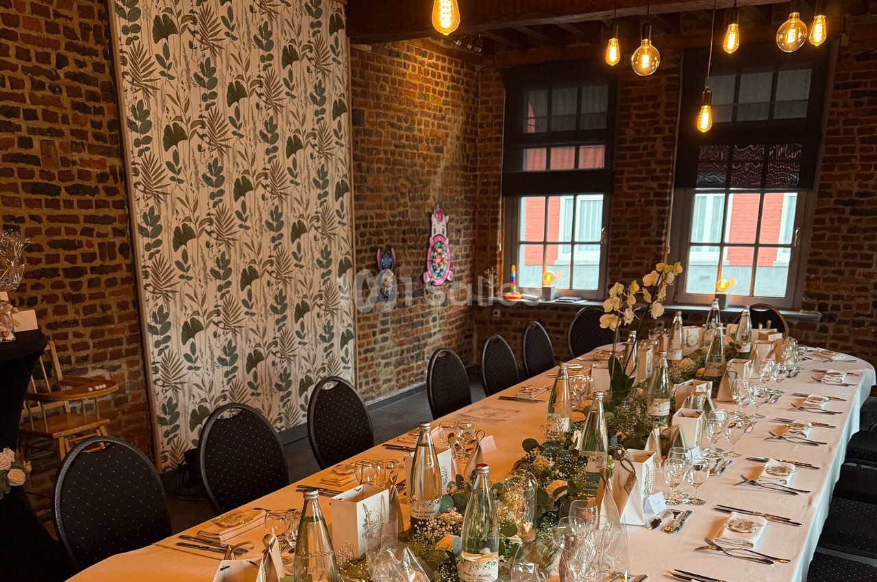 Table dressée pour un repas festif dans une salle en briques avec éclairage suspendu et décoration végétale.