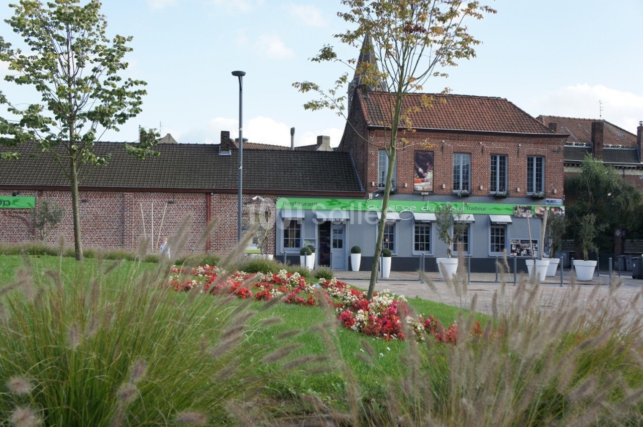 Façade d'un restaurant en briques rouges avec terrasse, entourée de parterres fleuris et d'arbres.