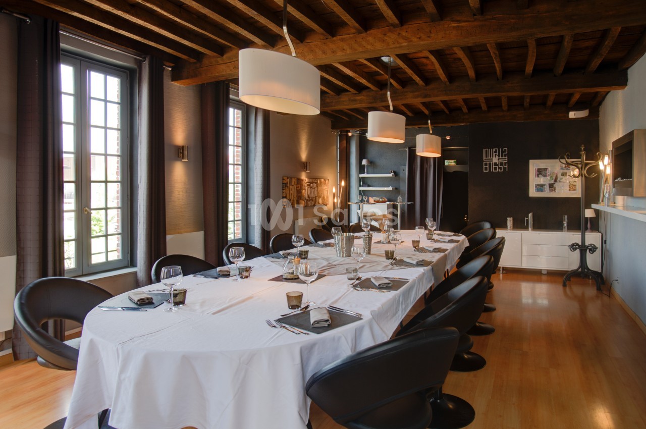 Salle à manger élégante avec une grande table dressée, chaises noires, plafond en bois et lumière naturelle.