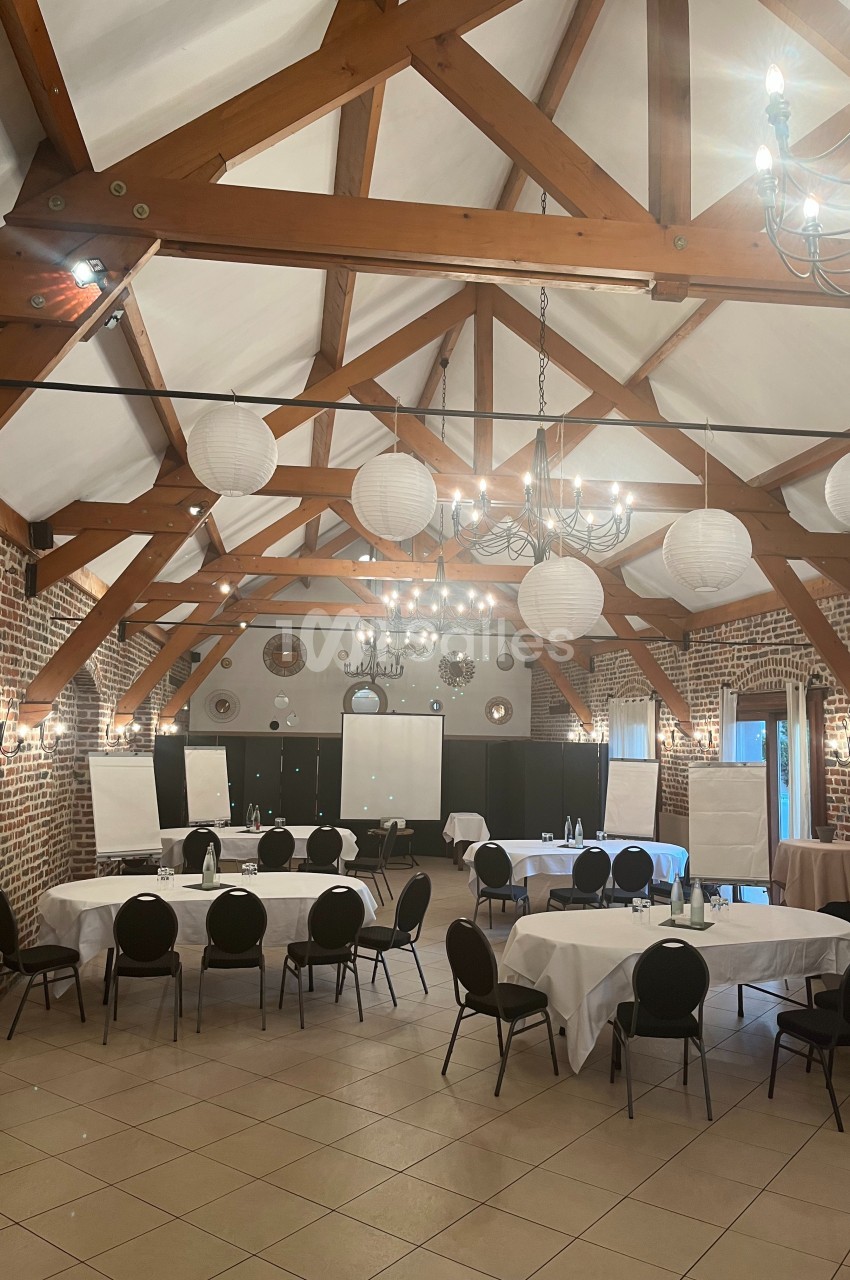 Salle de réunion spacieuse avec poutres apparentes, tables rondes et rectangulaires, chaises noires et décorations…