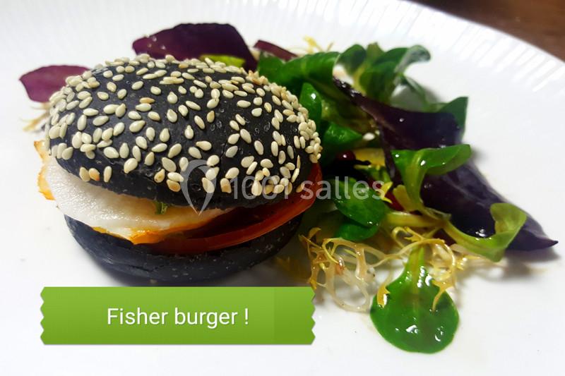 Burger au pain noir garni de poisson, tomate et salade, accompagné de jeunes pousses sur une assiette blanche.
