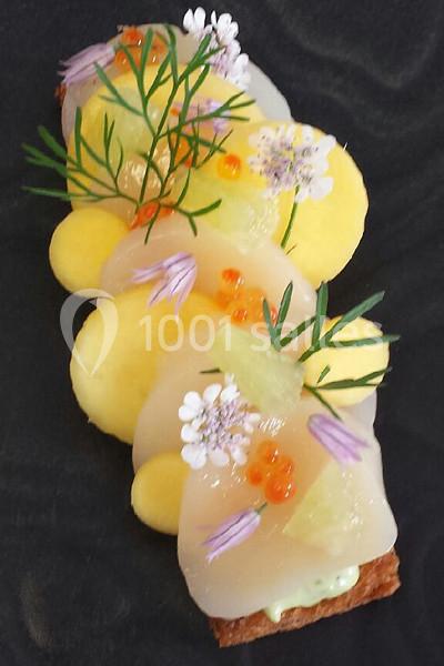 Tranche de pain garnie de carpaccio de Saint-Jacques, perles d'agrumes, fleurs comestibles et herbes fraîches.