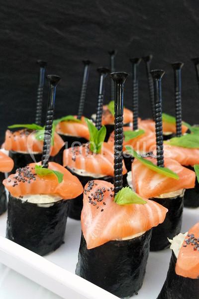 Sushis au saumon garnis de graines de pavot et de feuilles de basilic, présentés avec des piques noires.