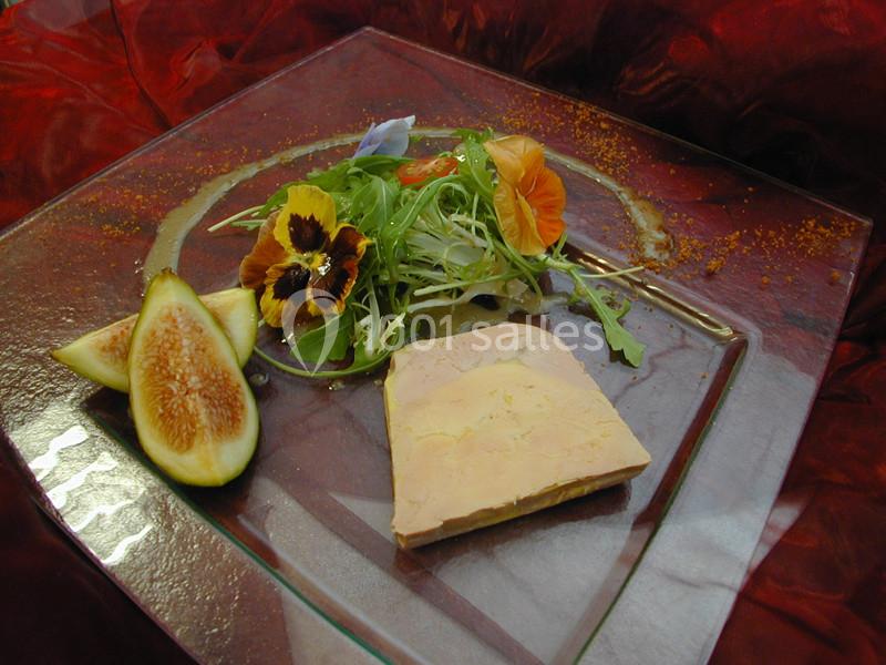 Assiette de foie gras accompagné de figues fraîches, salade verte et fleurs comestibles sur un fond rouge.