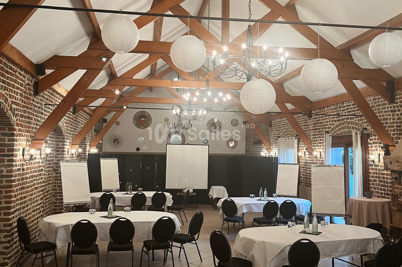 Salle de réunion avec tables rondes, chaises noires, tableaux de présentation et décorations en briques et bois.