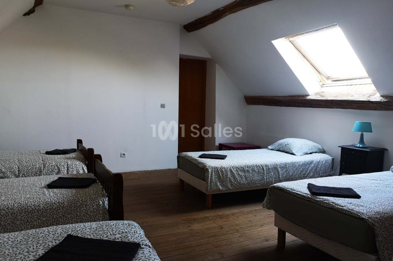 Chambre mansardée avec quatre lits simples, parquet en bois, fenêtre de toit et mobilier minimaliste.