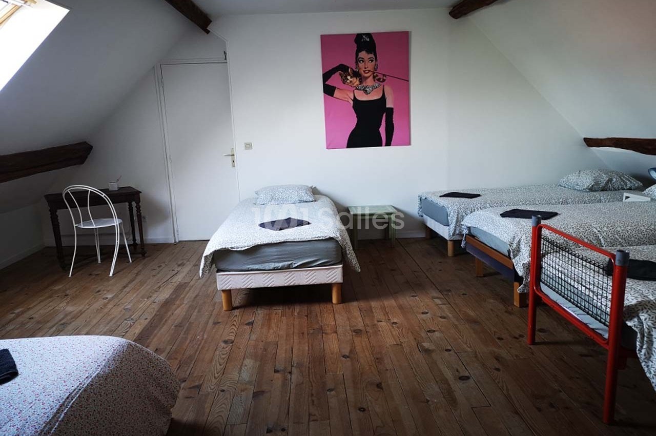 Chambre mansardée avec quatre lits simples, parquet en bois, bureau et affiche décorative sur le mur.