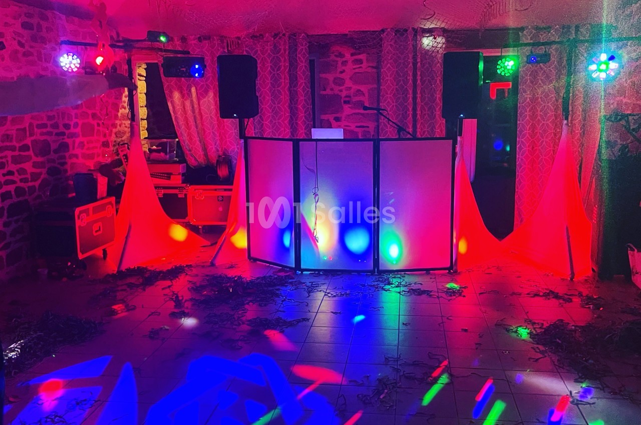 Salle de fête décorée avec des lumières colorées, un espace DJ et des rideaux en arrière-plan.