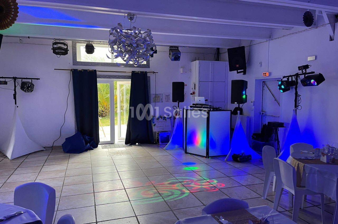 Salle de réception avec éclairage coloré, piste de danse, tables dressées et matériel de sonorisation installé.
