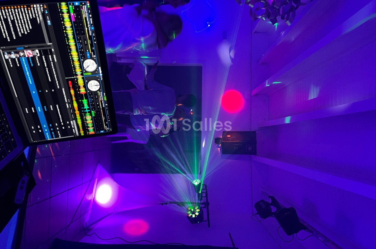 Salle de fête éclairée par des lumières colorées, avec une table de mixage visible au premier plan.