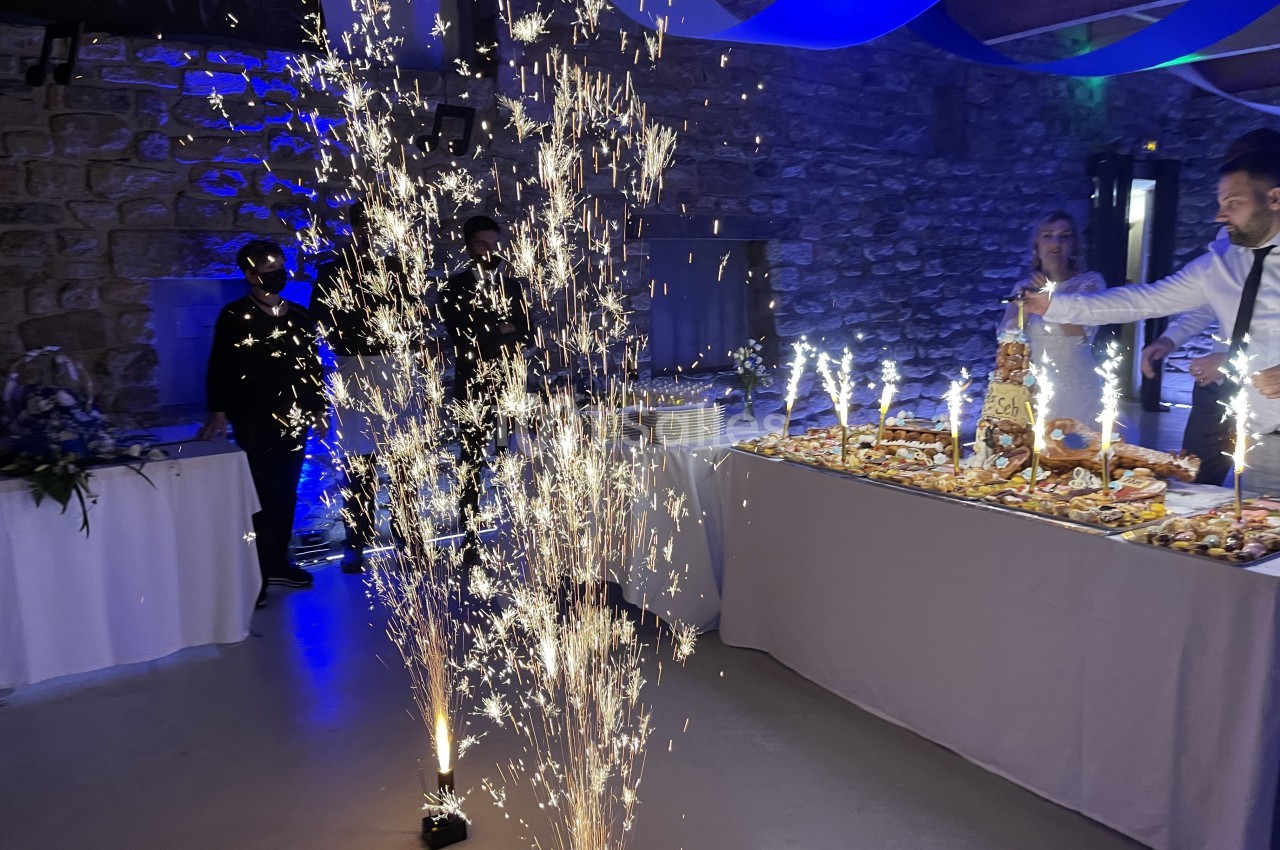 Des fontaines lumineuses illuminent une table de buffet garnie de desserts dans une salle en pierre décorée.