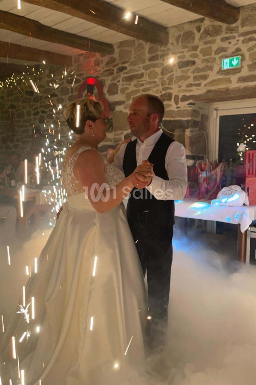 Un couple danse dans une salle en pierre illuminée, entouré d'effets de lumière et de fumée.