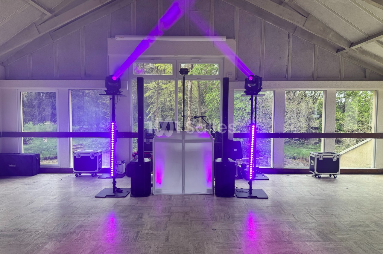 Installation de matériel de sonorisation et éclairage violet dans une salle avec de grandes fenêtres donnant sur un espace…