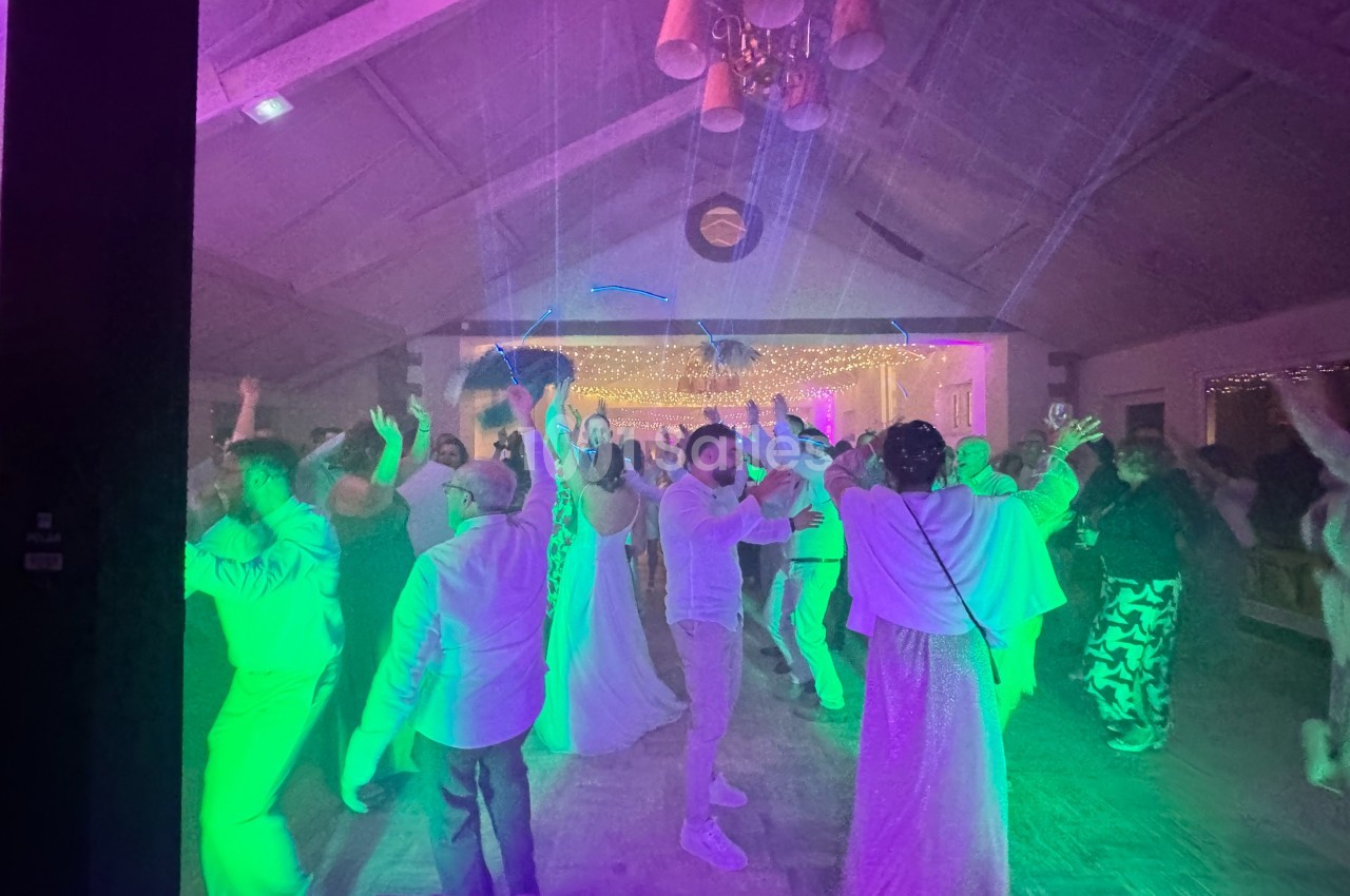 Personnes dansant sous des lumières colorées dans une salle décorée, ambiance festive et animée.