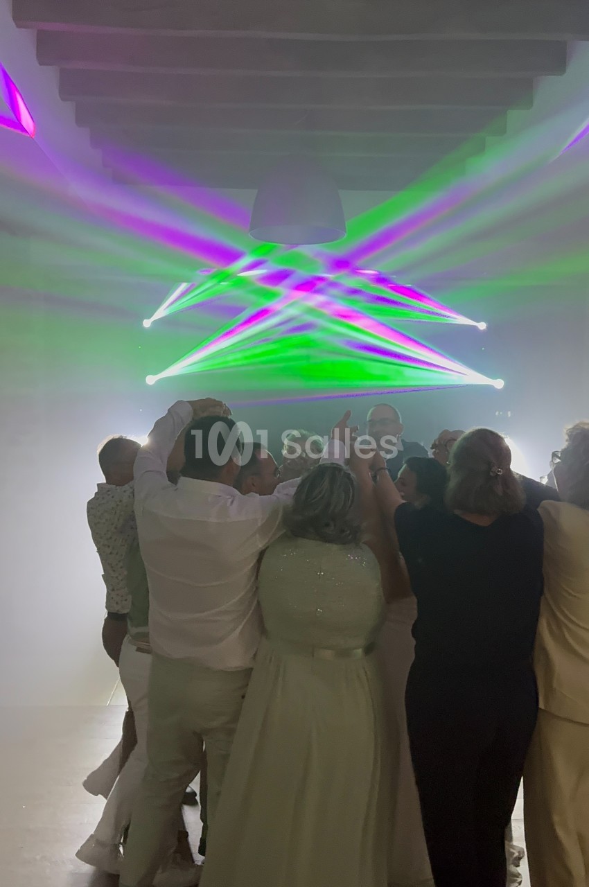 Groupe de personnes dansant sous des lumières colorées dans une salle sombre avec un plafond en bois.
