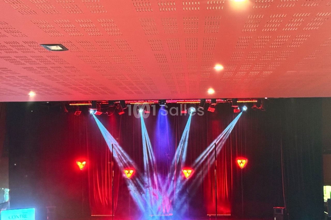Scène de spectacle avec éclairages rouges et bleus, rideaux noirs en arrière-plan et projecteurs dirigés vers le centre.