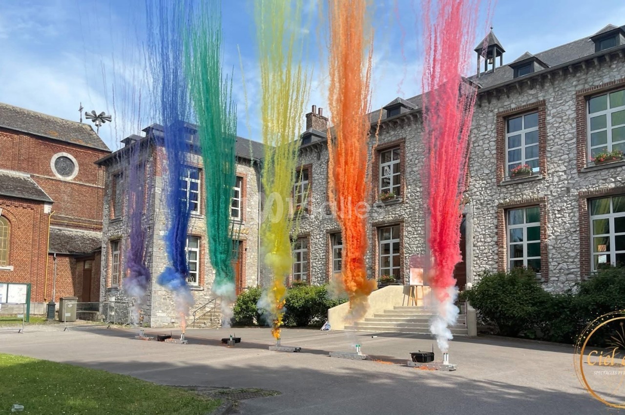 Jets de poudre colorée s'élevant devant un bâtiment en pierre avec des fenêtres et une cour pavée.