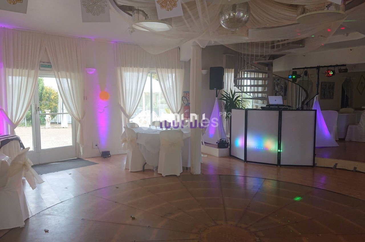 Salle de réception lumineuse avec piste de danse circulaire, tables dressées et éclairages colorés près d'une baie vitrée.