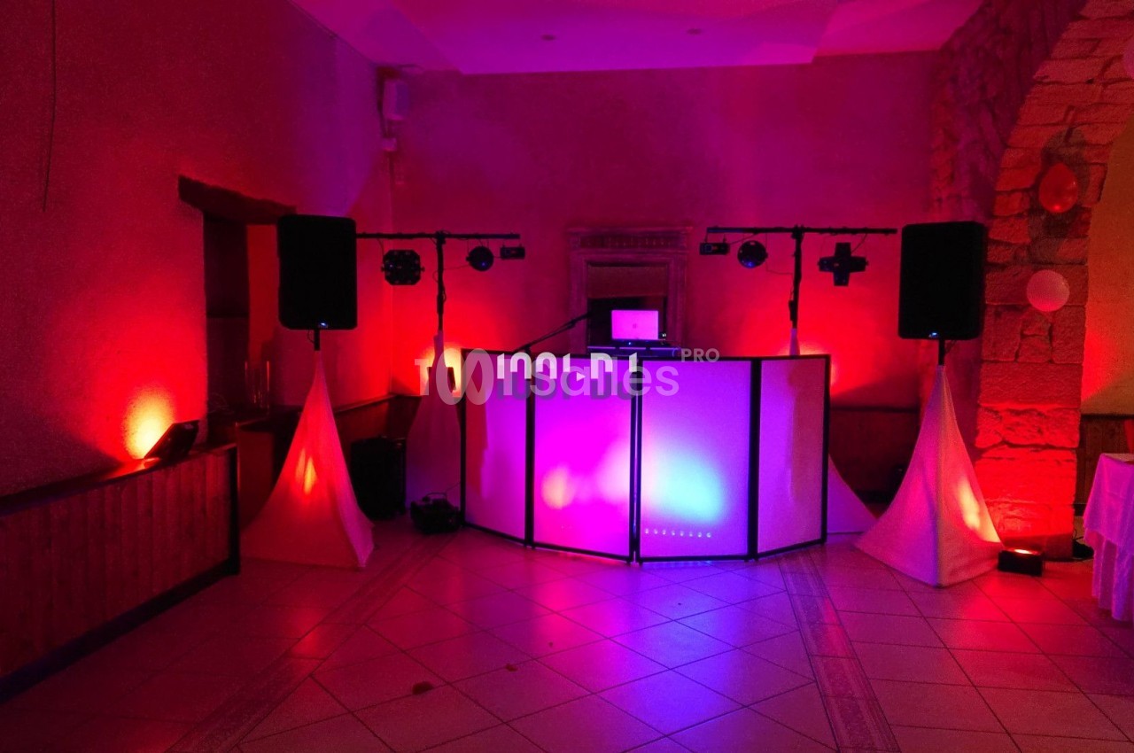 Salle de réception avec éclairage rouge et violet, équipement de sonorisation et cabine de DJ au centre.