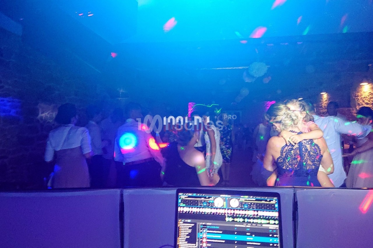 Des personnes dansent dans une salle sombre éclairée par des lumières colorées, avec une console de DJ au premier plan.