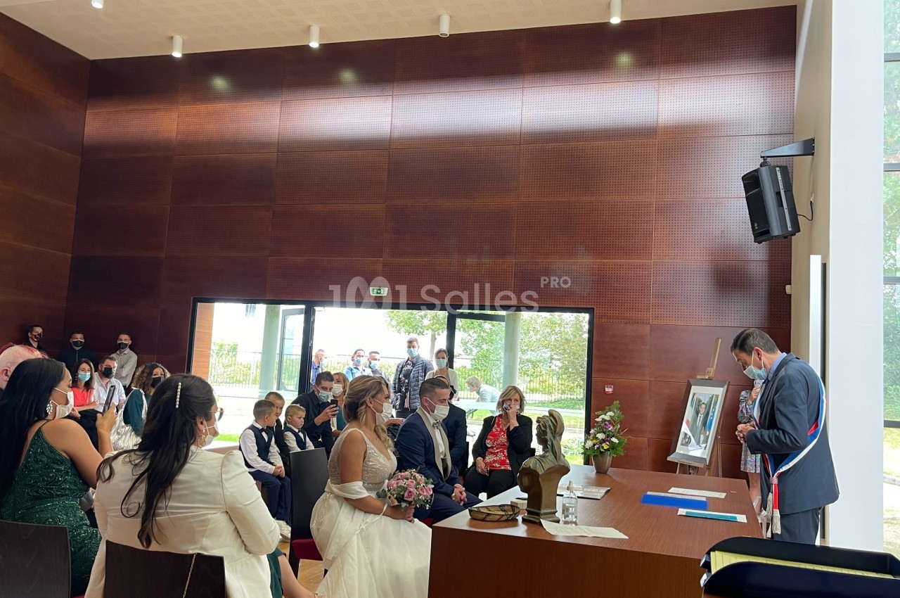 Un couple assis face à un officier municipal lors d'une cérémonie de mariage dans une salle lumineuse.