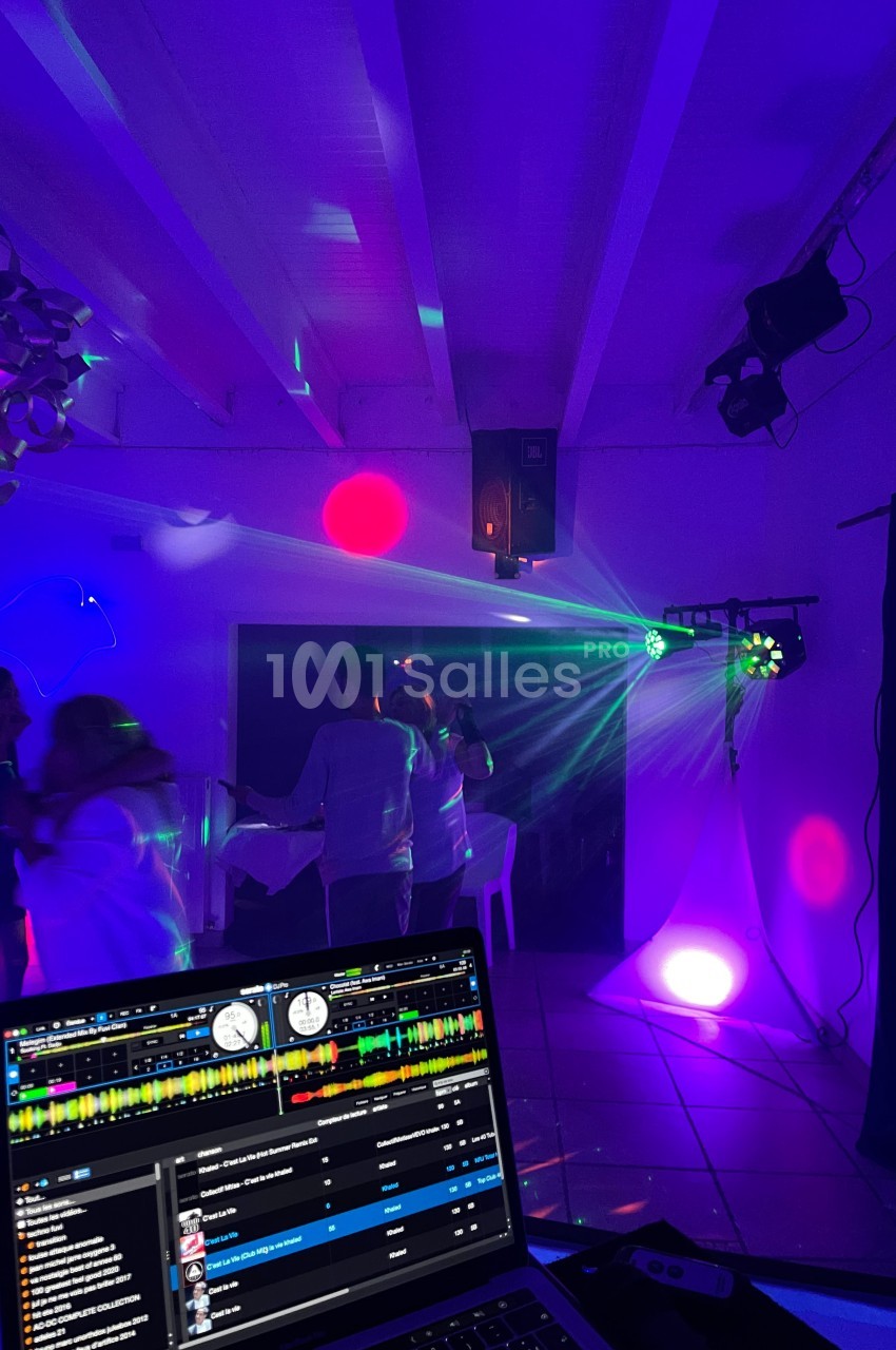 Des personnes dansent sous des lumières colorées dans une salle, avec un ordinateur affichant un logiciel de mixage au…