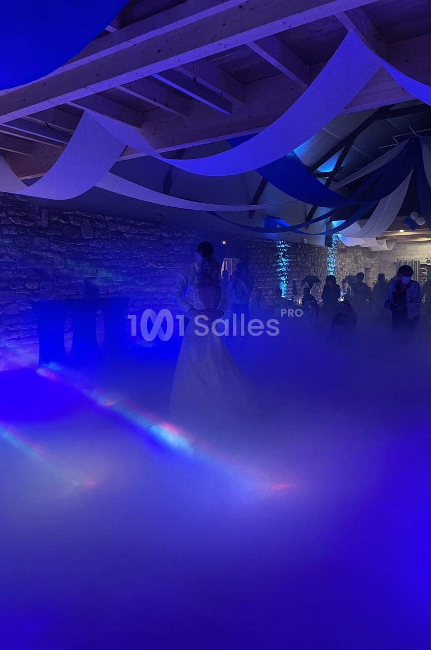 Un couple danse dans une salle éclairée par des lumières bleues, entouré d'un épais brouillard au sol.
