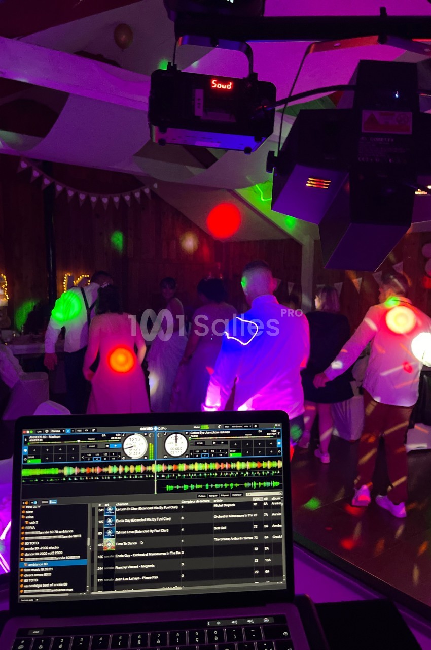 Des invités dansent sous des lumières colorées lors d'une soirée festive, avec une console DJ en premier plan.