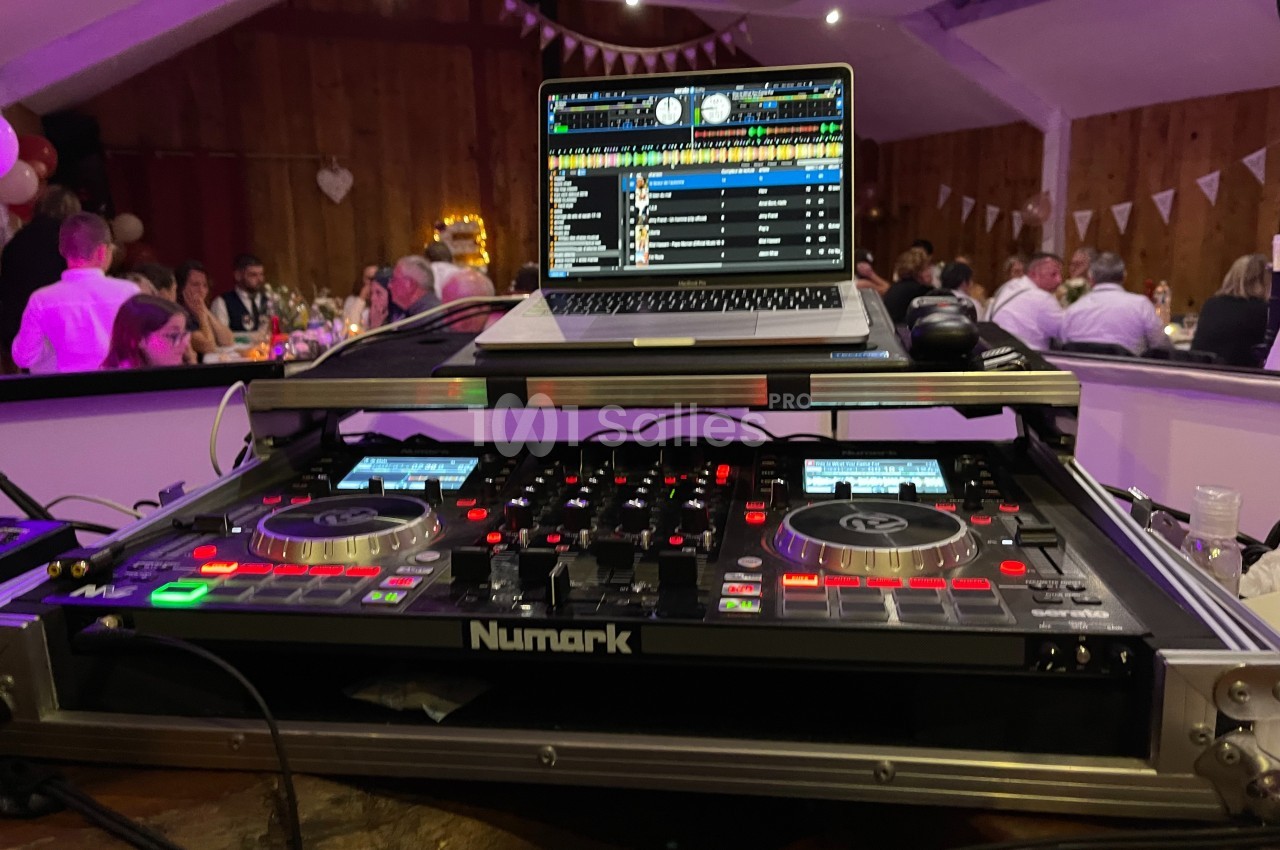 Table de mixage avec ordinateur portable affichant une playlist, installée dans une salle décorée pour un événement.