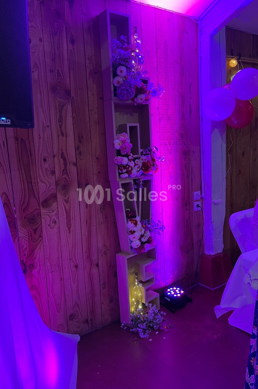 Étagère en bois formant le mot ’LOVE’, décorée de fleurs et éclairée par une lumière violette dans une salle festive.