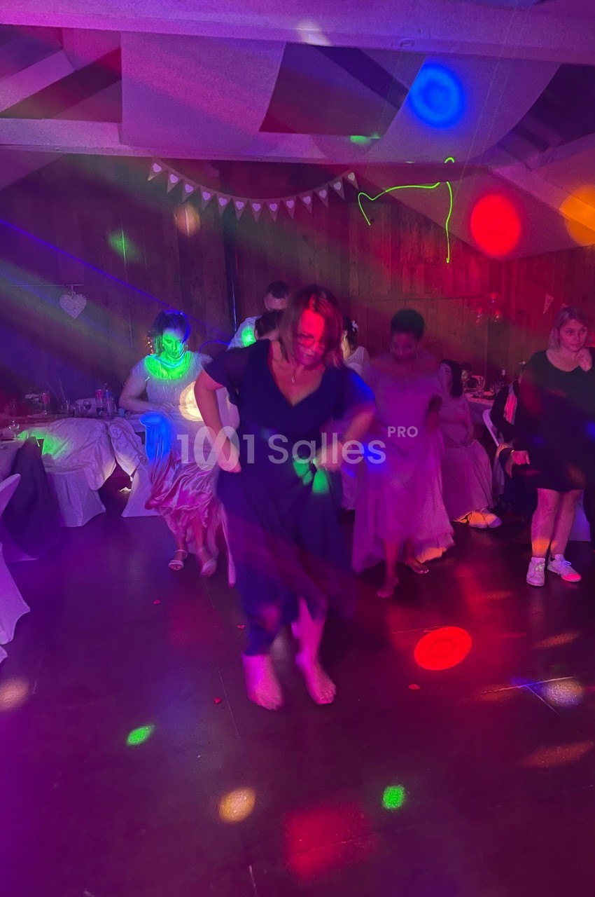 Des personnes dansent dans une salle décorée, éclairée par des lumières colorées et festives.