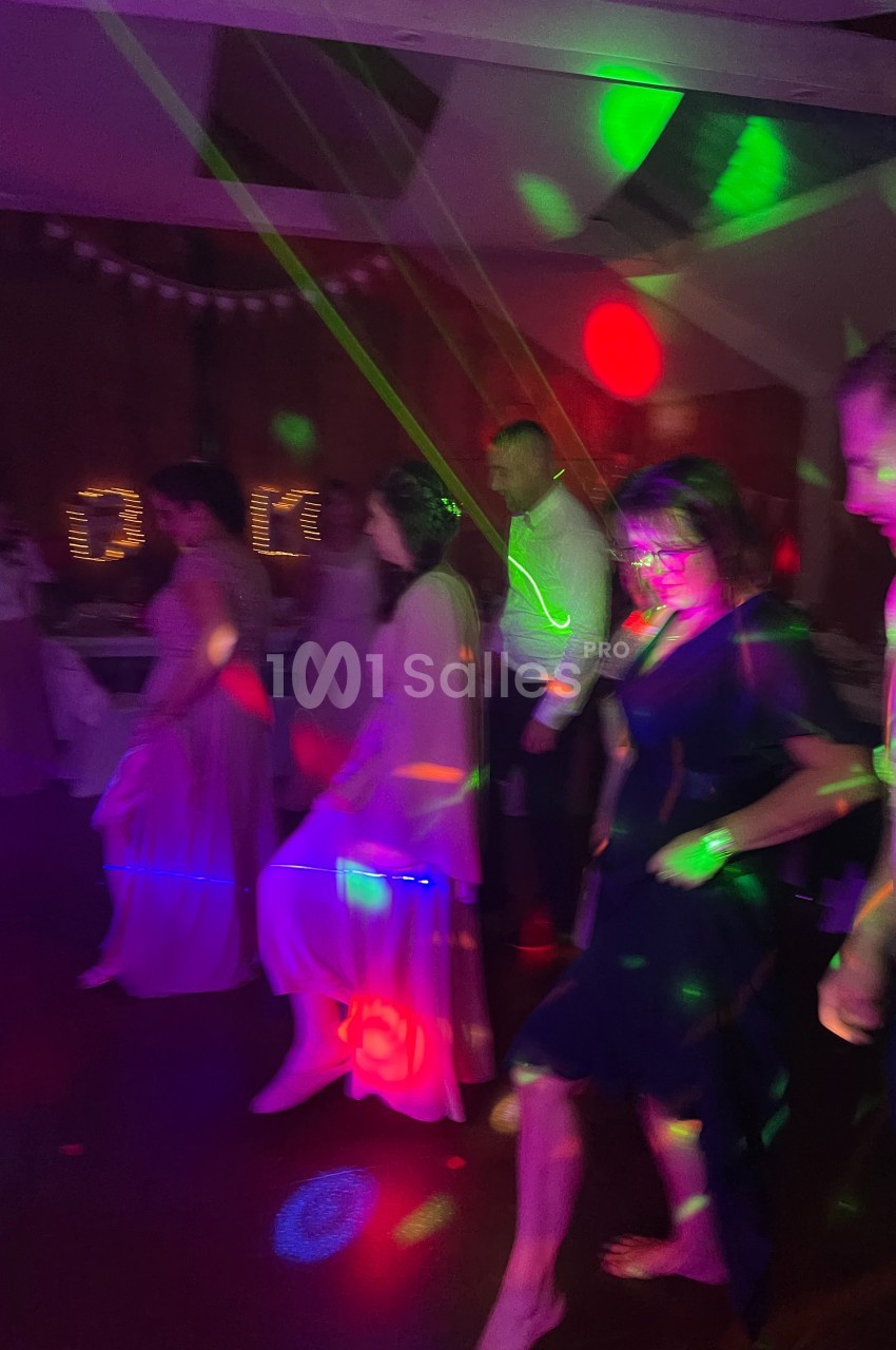 Des personnes dansent en ligne dans une salle sombre éclairée par des lumières colorées.